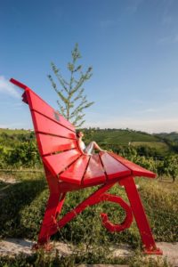 Big Bench in Piedmont in red with lady sitting on it taking sun within the vineyards